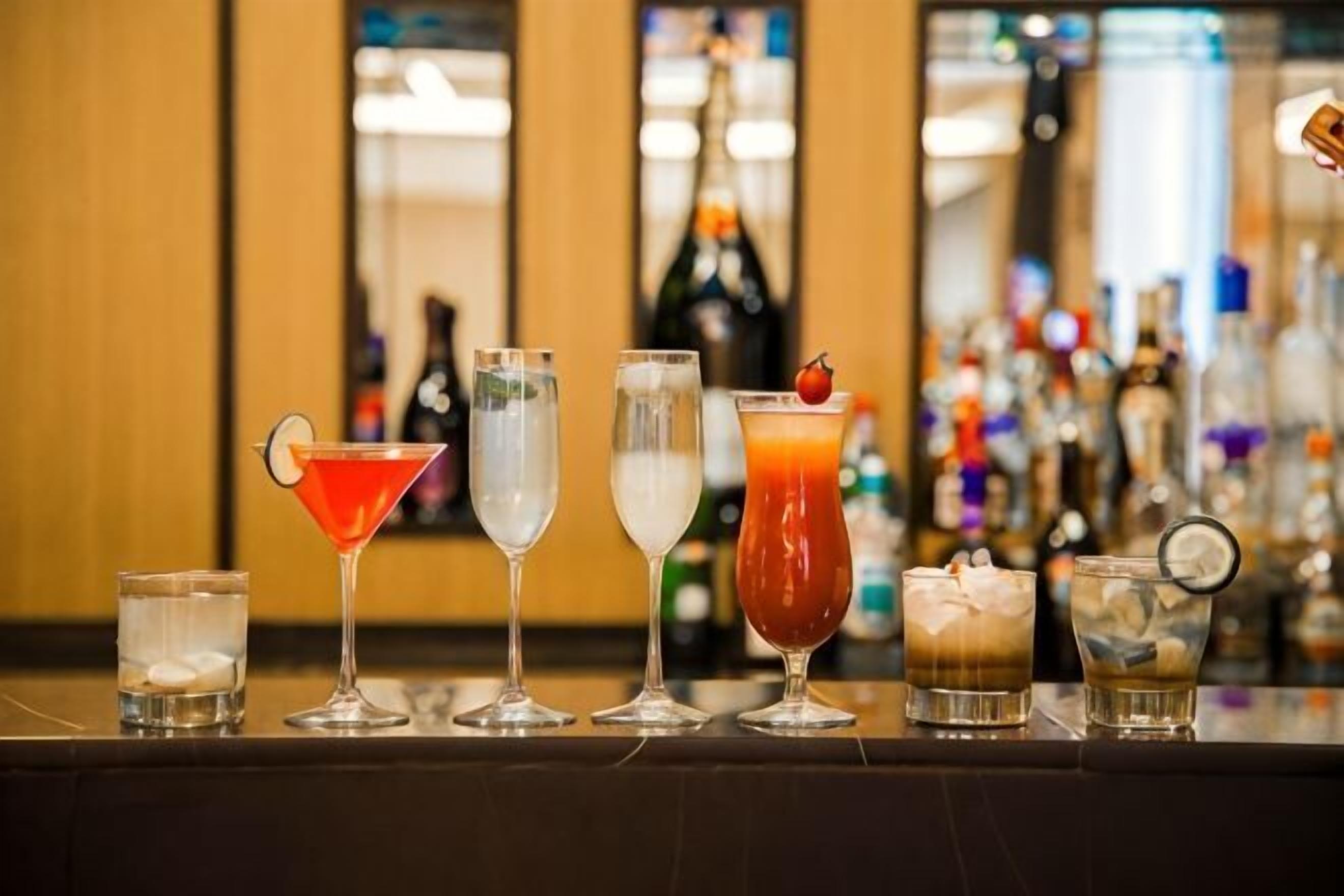 A bar with various drinks, a bottle of wine, and a bartender's hand.