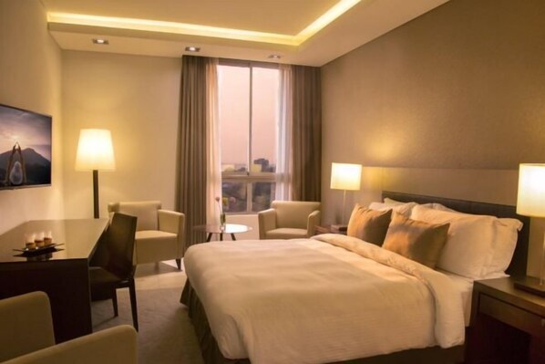 Une chambre d’hôtel avec un grand lit, deux tables de chevet, un bureau avec une chaise, deux lampes et une fenêtre avec des rideaux.