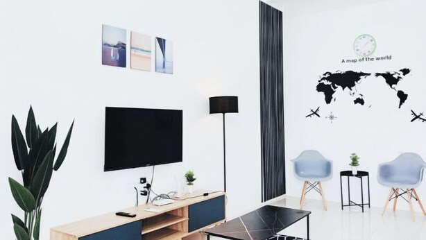 A modern living room with a flat-screen TV, a wooden entertainment unit, a black floor lamp, and a world map wall decal. - D' Splash Garden Homestay Baling (Baling)