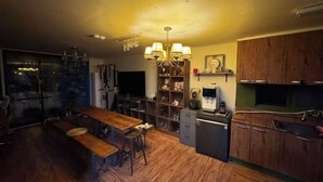 Eine Küche mit Holzschränken, einem Esstisch mit Bänken, einer Chandelierleuchtre und einem Kühlschrank.