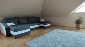 A modern living room with a sectional sofa, a light blue rug, and a potted plant. - Apartment 'Ferienwohnung Haak' with Private Terrace, Balcony and Wi-Fi (Dörpen)