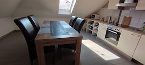 A dining area with a wooden table and chairs, a kitchen with a microwave and oven, and a skylight.