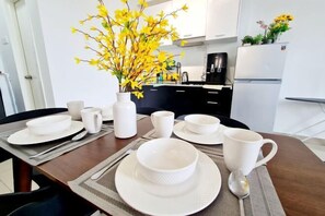 A dining table set with white dishes and cups, a vase with yellow flowers, and a kitchen in the background. - Broad 7 Guest Scott Garden / Old Klang Road / Bangsar South / Mid Valley / Kuala Lumpur (Kuala Lumpur)