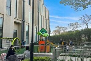 Un espacio al aire libre con un parque infantil, un edificio con ventanas amplias y un cielo despejado.