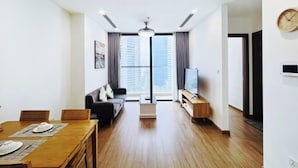 A modern living room with a dining area, a sofa, a TV, and a large window. - Vinhomes Skylake by TA Home – Premium Hanoi Apartment (Hanoi)