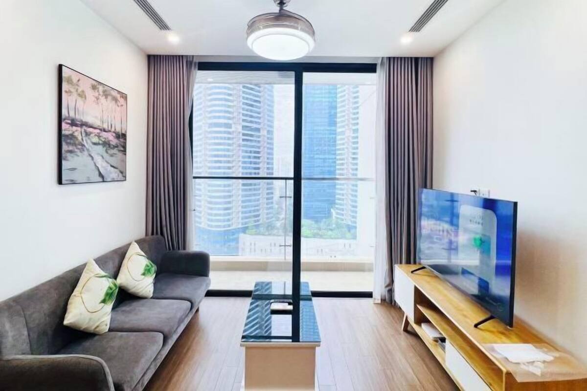 Una sala de estar moderna con un sofá, un televisor sobre un mueble de madera, un cuadro en la pared y un ventanal con cortinas.