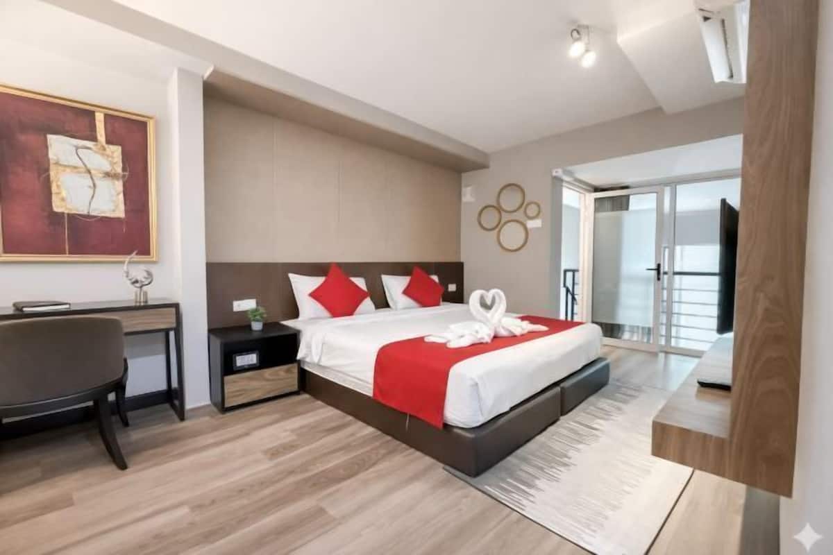 A modern hotel room with a bed, desk, and a view of the outdoors.
