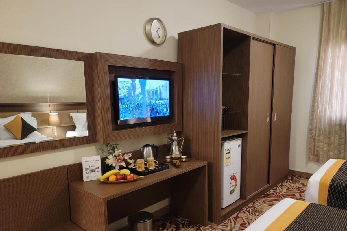 Een hotelkamer met een bed, een bureau met een televisie, een kast en een kleine koelkast.