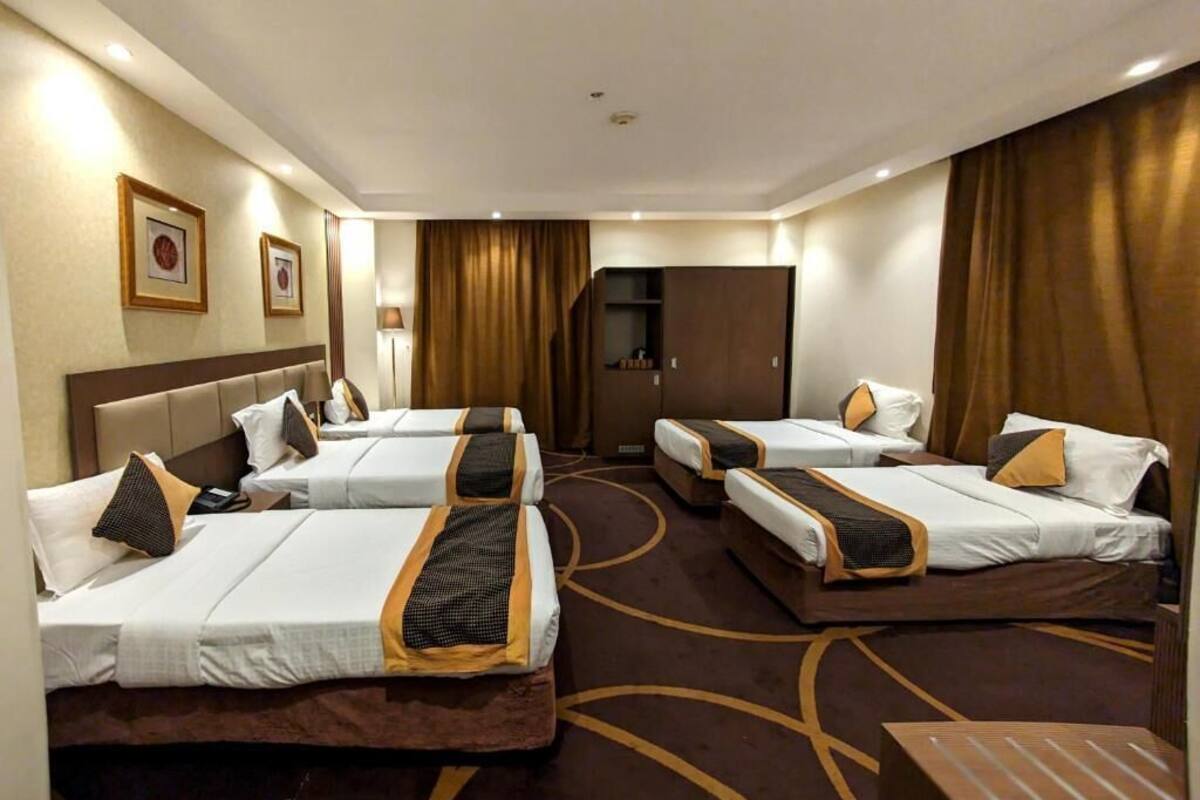 A hotel room with three beds arranged in a row, a wardrobe, and a desk.