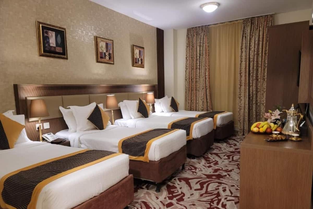 A hotel room with three beds, a desk, and a patterned carpet.