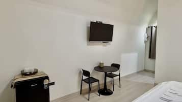 A hotel room with a bed, a TV mounted on the wall, a small table with chairs, and a minibar.