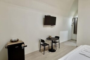 A hotel room with a bed, a TV mounted on the wall, a small table with chairs, and a minibar. - Skyinn Resort (Khok Samrong)