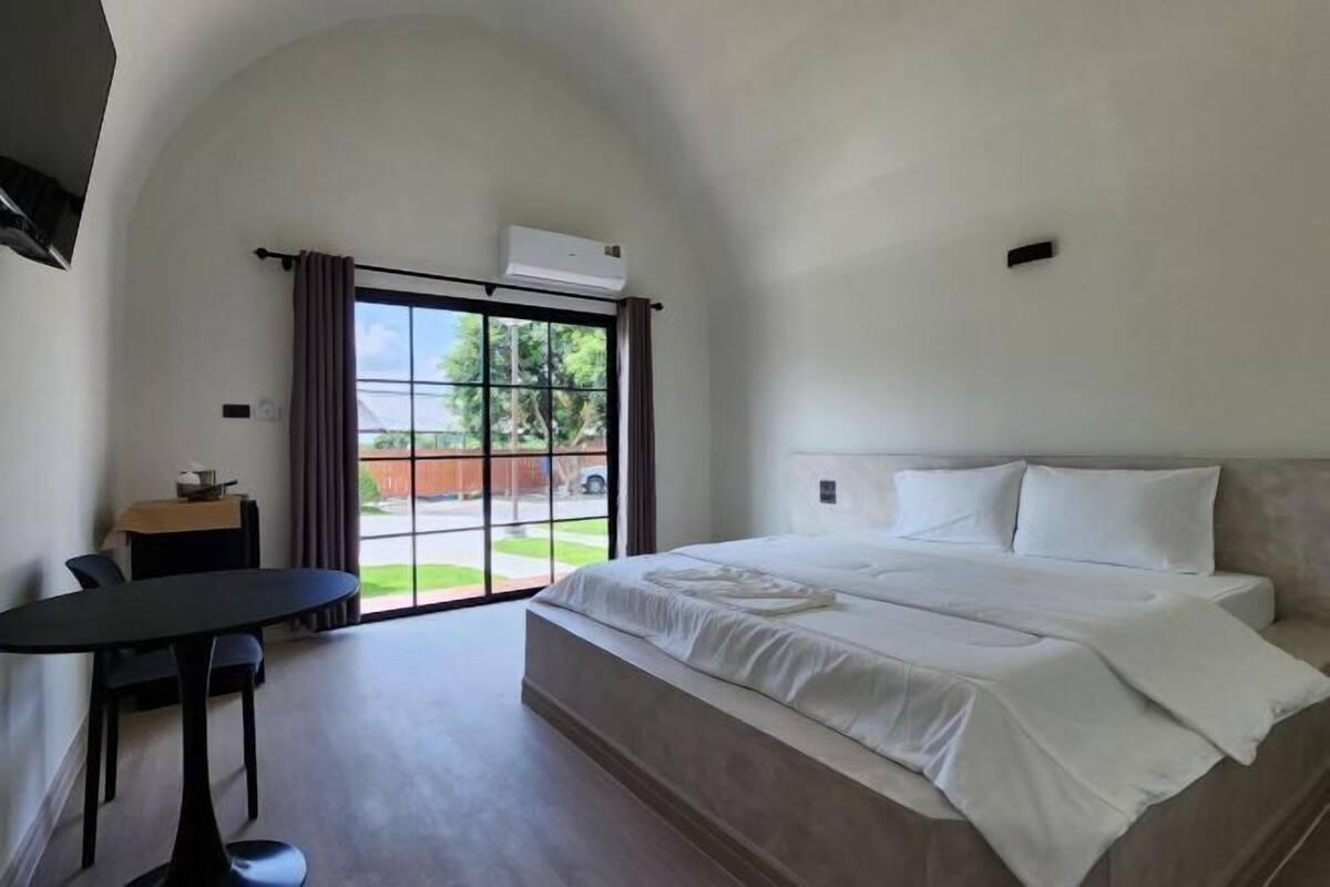 Ein Schlafzimmer mit einem großen Bett, einem kleinen Tisch und einem Fenster mit Vorhängen.