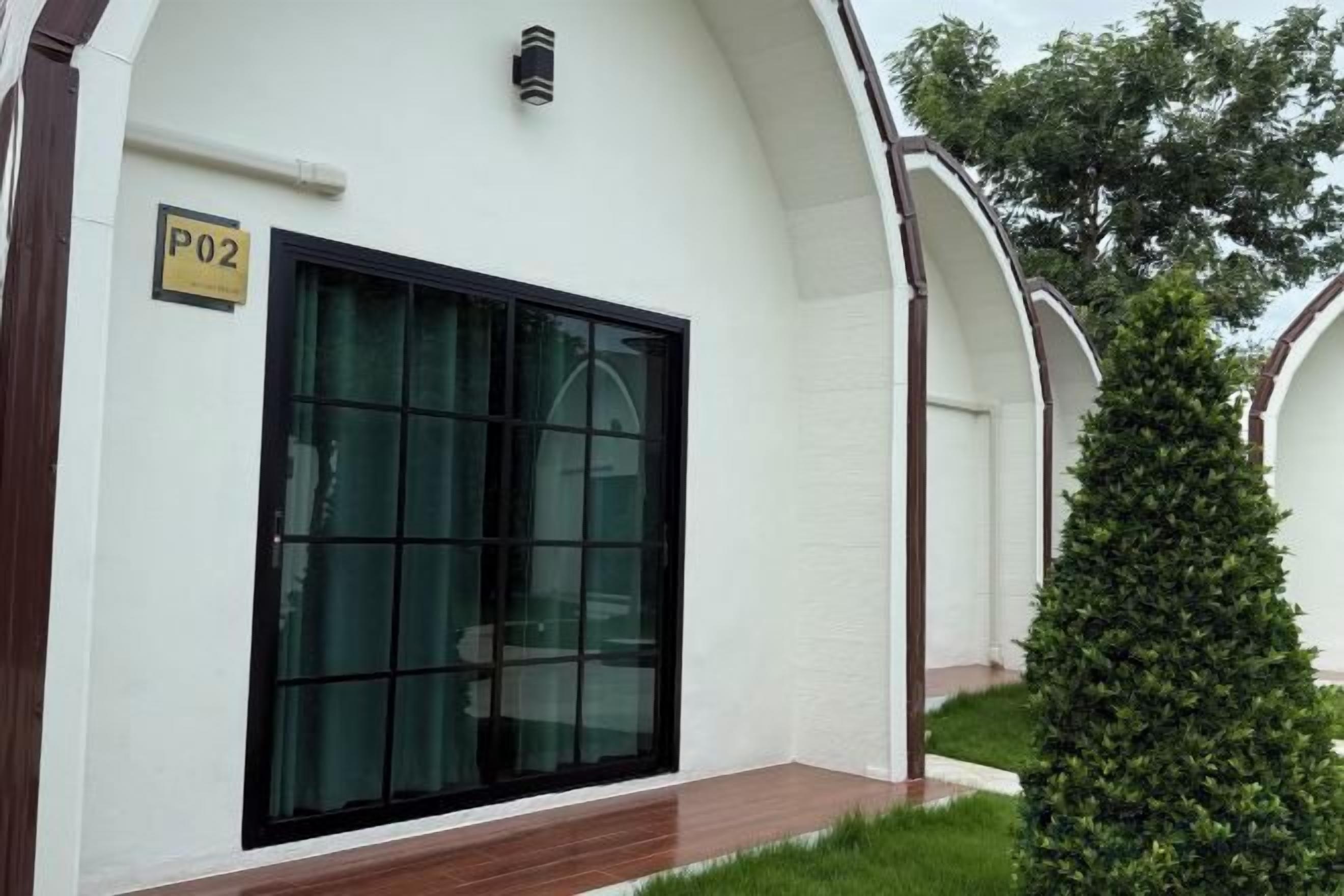 A building with a large glass door, a sign indicating room number P02, and a small green bush in front.