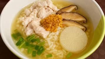 A bowl of soup with chicken, mushrooms, corn, and green onions.