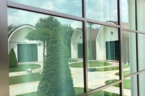 Un edificio moderno con un diseño simétrico, que presenta un patio central con un césped bien cuidado y un árbol alto y cónico.