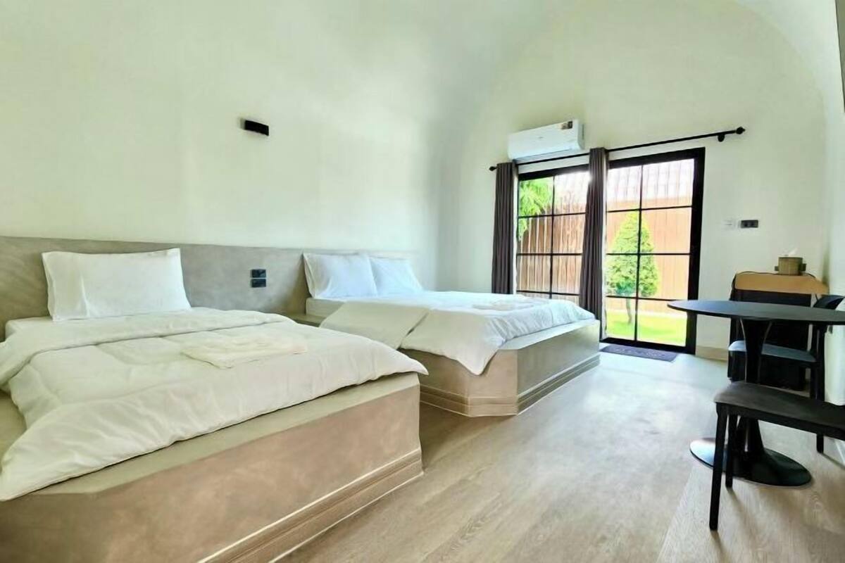 Ein Schlafzimmer mit zwei Betten, einem Tisch und Blick ins Freie.
