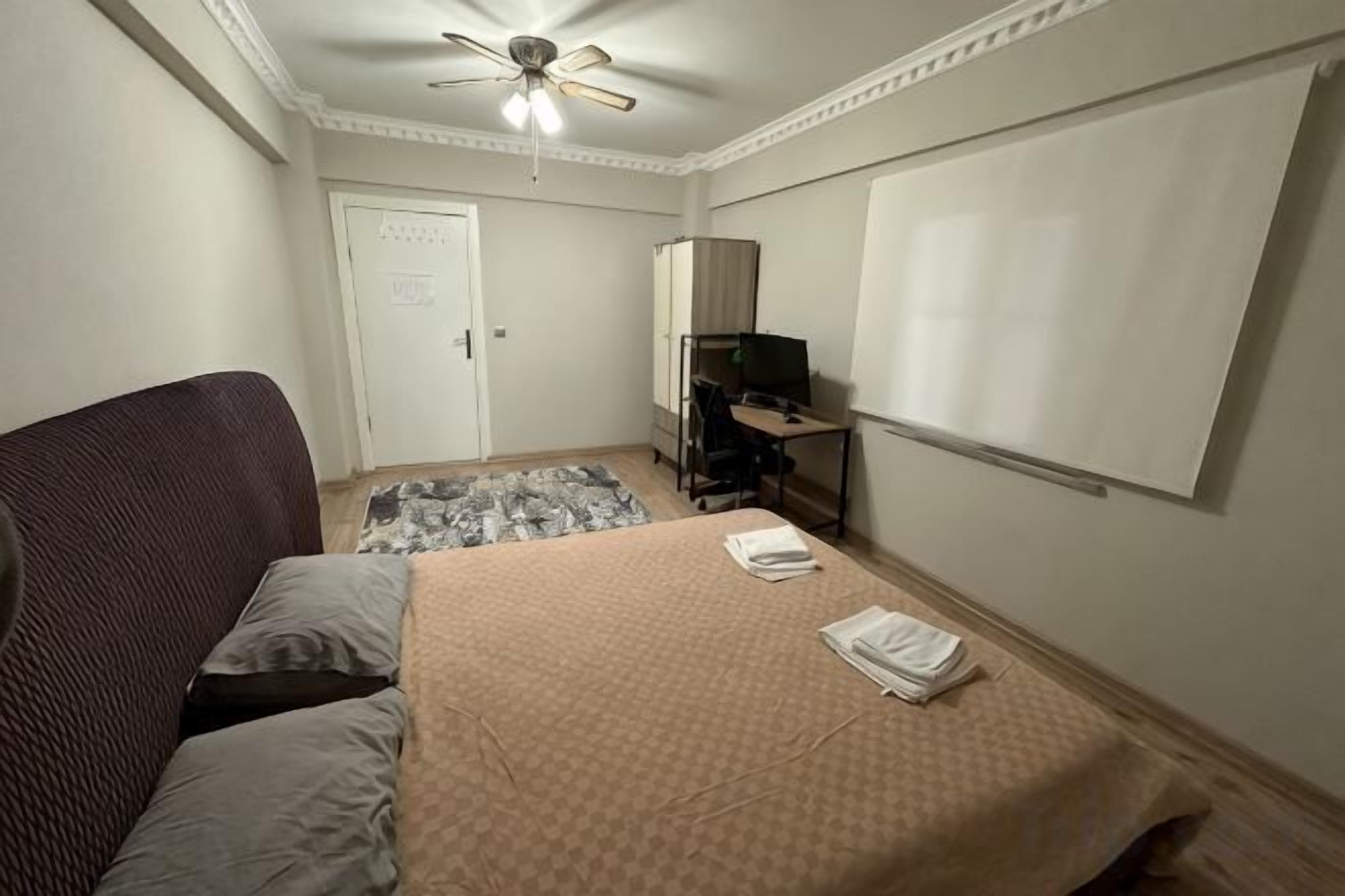 Una habitación de hotel con cama, escritorio, silla, ventilador de techo y televisión.