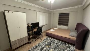 Un dormitorio con cama, escritorio, silla, armario y ventilador de techo.
