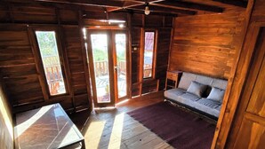 A cozy cabin with a wooden interior, a sofa, a table, and a view through the windows. - Munduk Terrace By Zuzu (Munduk)