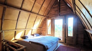 A cozy attic bedroom with a bed, wooden beams, and a view of the outdoors. - Munduk Terrace By Zuzu (Munduk)