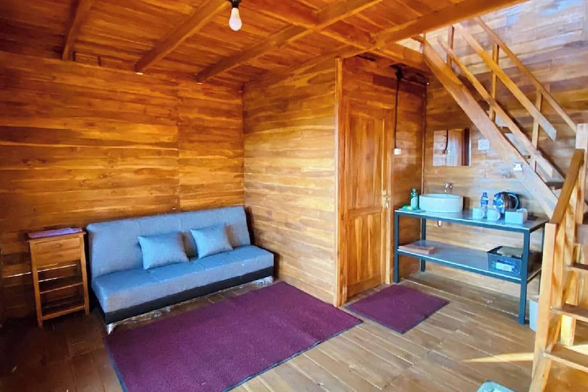 Ein gemütliches Blockhauss-Interieur mit Holzbalkendecke, einer Couch, einem kleinen Tisch und einer Treppe.