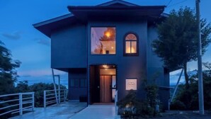 A modern two-story building with a large window on the upper floor, a small arched window on the ground floor, and a sign indicating a restaurant or cafe. - The Villas〜atami amazing ocean view〜 (Atami)
