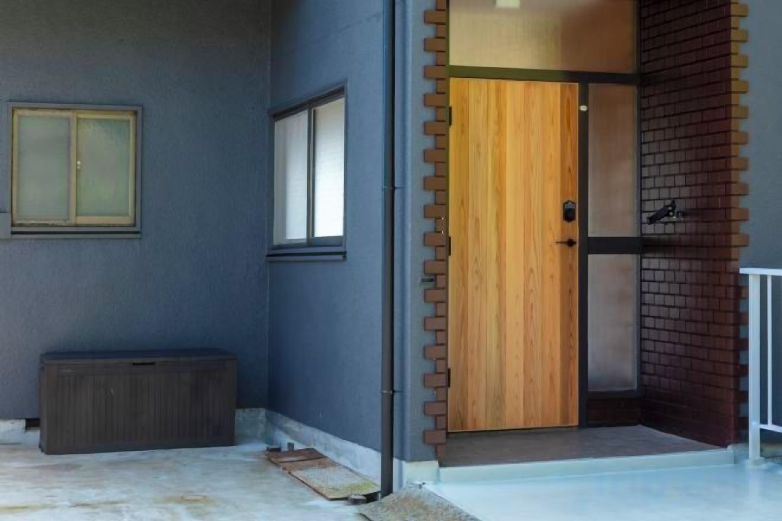 A modern entrance with a wooden door, a small window, and a concrete step leading to a brick wall.