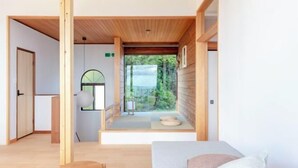 A room with a bed, a small table, a bench, and a view of greenery outside. - The Villas〜atami amazing ocean view〜 (Atami)