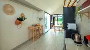 A modern kitchen with wooden stools, a coffee maker, and a view through the glass door. - Baan Ga-cha (Chiang Rai)