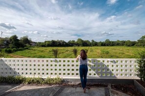 A person standing on a balcony overlooking a green field with a white fence. - Baan Ga-cha (Chiang Rai)
