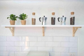 Une étagère de cuisine avec des plantes en pot, une machine à café et des pots à épices.