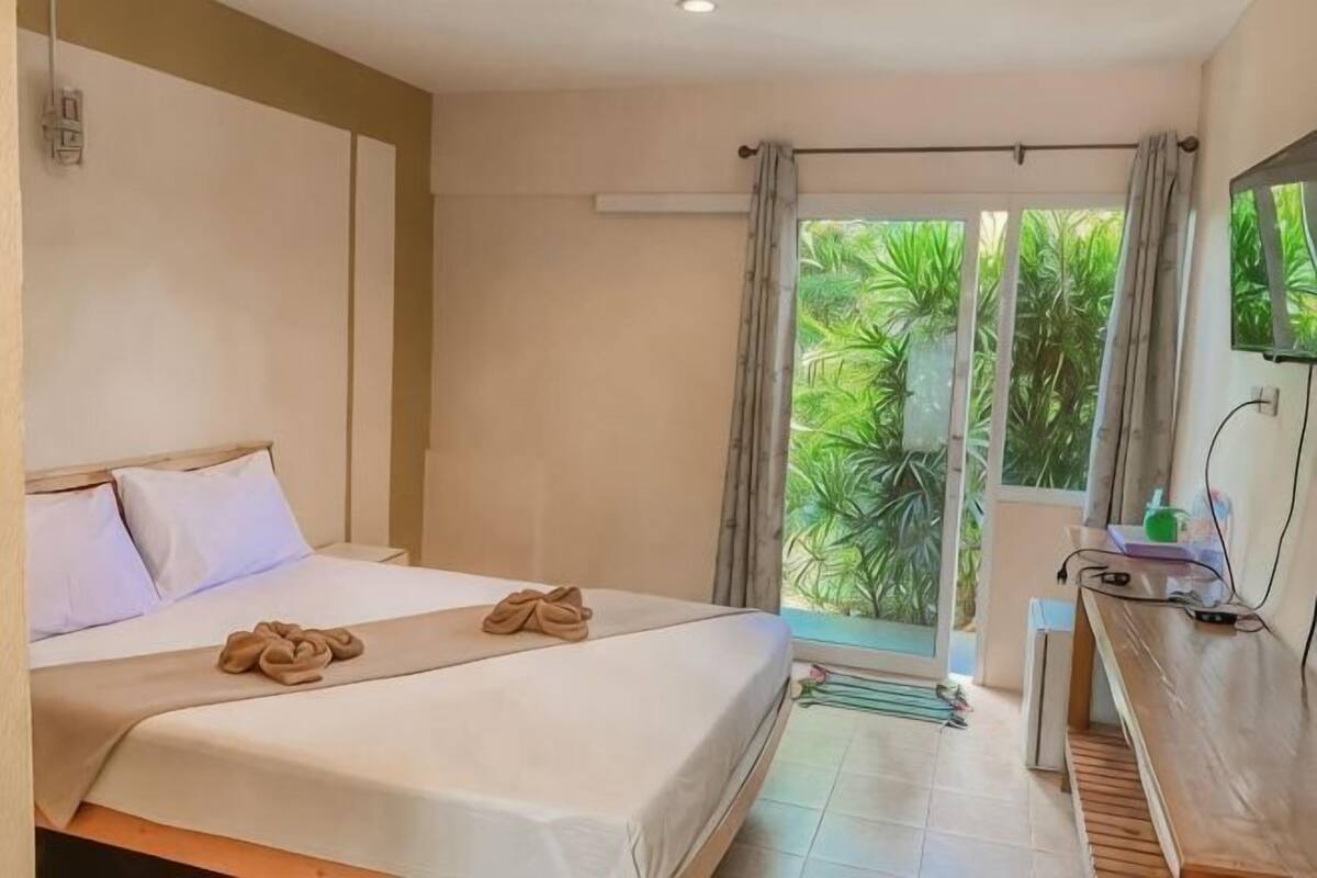 A hotel room with a bed, a desk, and a view of greenery.