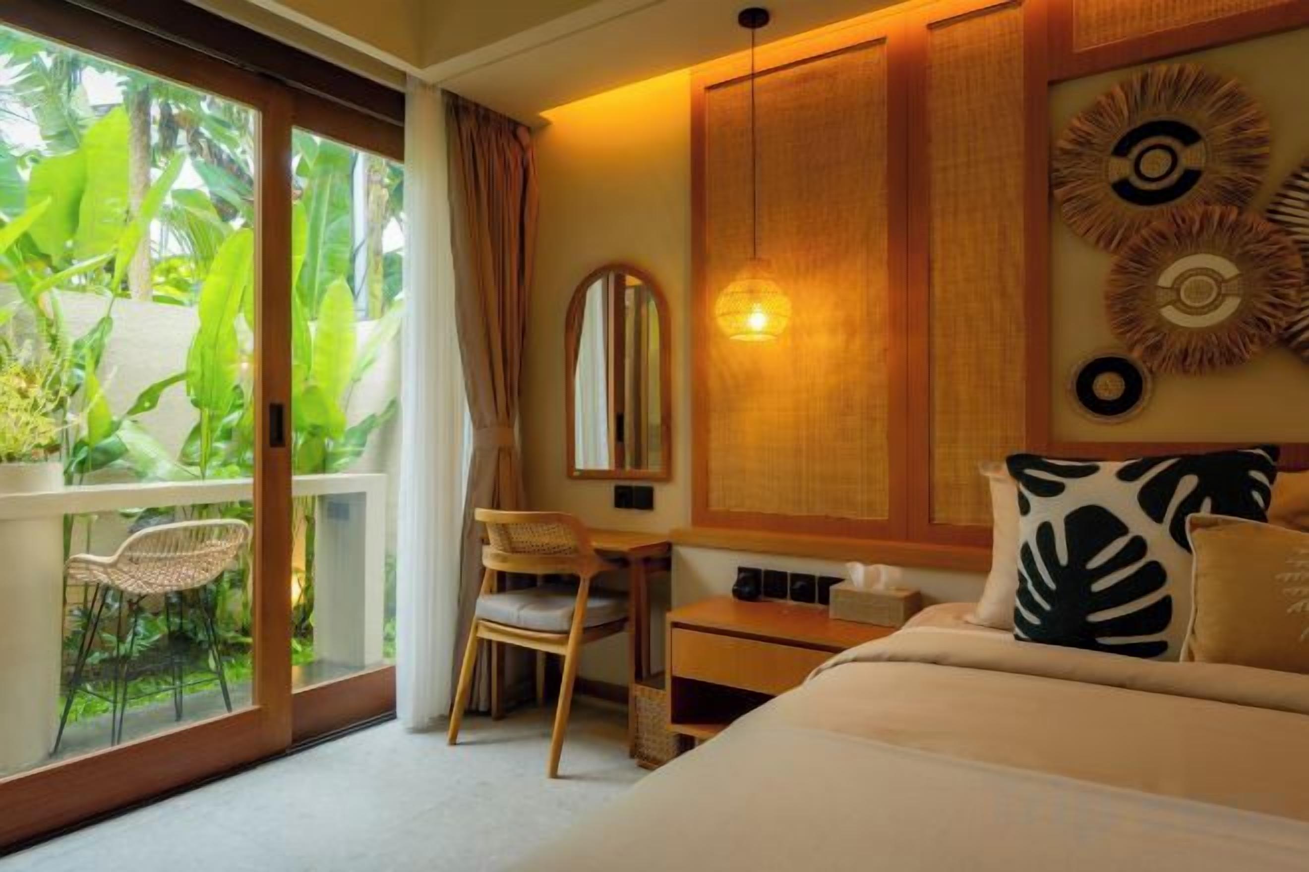 Habitación de hotel con cama, escritorio, silla y ventana grande con vistas a zonas verdes.
