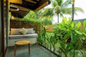 Un espace extérieur accueillant, aménagé avec un canapé et une petite table, entouré d’une végétation luxuriante et d’une clôture en bois.