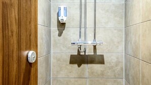 A shower with a handheld showerhead, a soap dispenser, and a wooden door. - Holiday Inn TAUNTON M5, JCT.25 by IHG (Taunton Deane District)