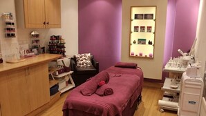 A room with a massage table, shelves with bottles, a chair, and a counter. - Holiday Inn TAUNTON M5, JCT.25 by IHG (Taunton Deane District)