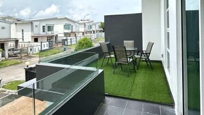 A modern balcony with a glass enclosure, a small table with chairs, and a view of neighboring houses. - d'Fun Desaru 16-20pax Private pool / BBQ / KTV (Bandar Penawar)
