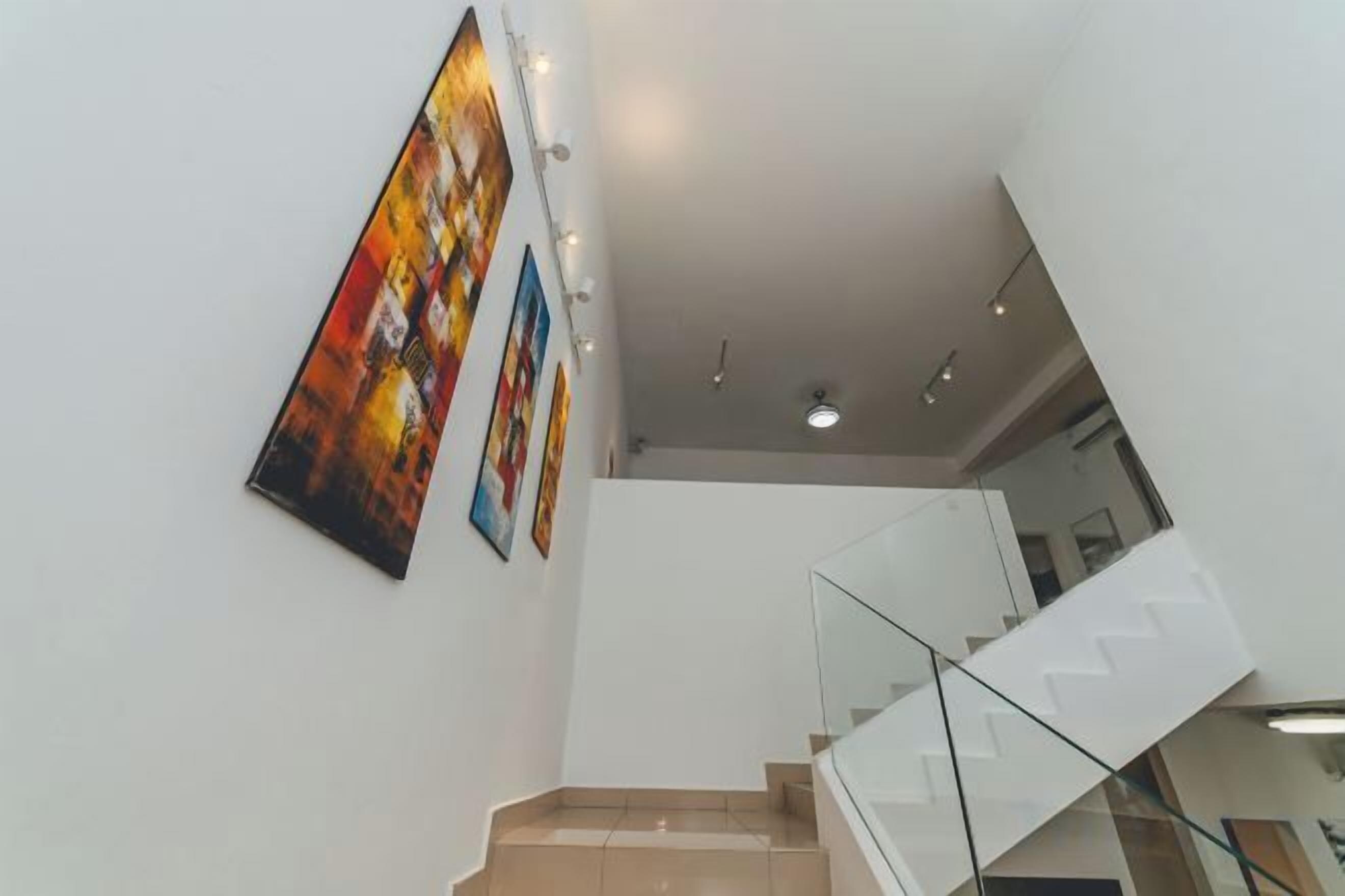 A modern staircase with glass railings and a white wall with three framed artworks.