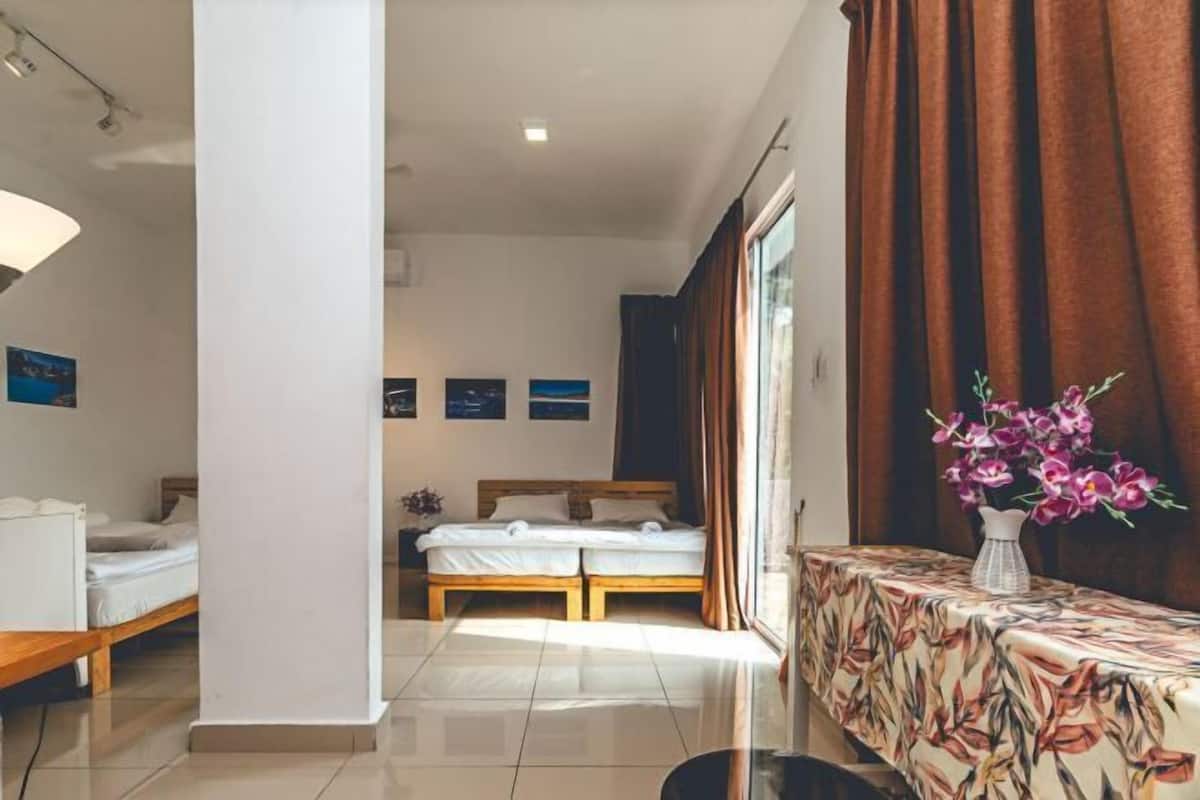 A hotel room with a bed, a small table with a floral tablecloth, and a window with curtains.