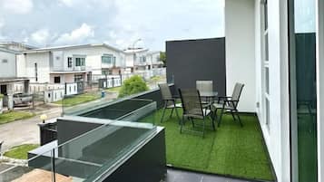 A balcony with a glass enclosure, a small table, and chairs, overlooking a residential area with houses.