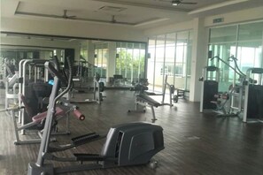 Ein geräumiger Fitnessraum mit verschiedenen Trainingsgeräten, großen Fenstern und einem Holzboden.