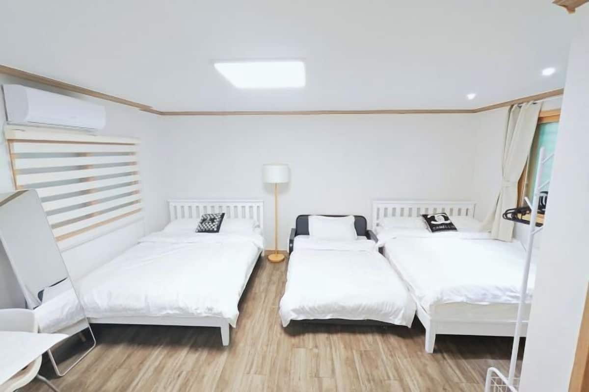 A room with three beds, a desk, a lamp, and a radiator.