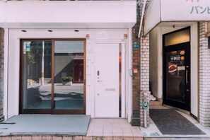 Une entrée d’immeuble avec une porte en verre, un petit espace extérieur aménagé en coin salon et un escalier bien visible menant à l’entrée.