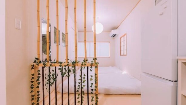 A room with a bed, a white refrigerator, and a bamboo partition with greenery. - “puff” Shinsaibashi Cloud House with Private Sauna (Osaka)