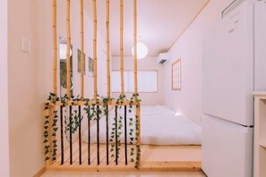 A room with a bed, a white refrigerator, and a bamboo partition with greenery. - “puff” Shinsaibashi Cloud House with Private Sauna (Osaka)