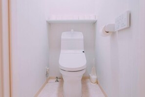 Een kleine, witte badkamer met een toilet, een toiletrolhouder en een zichtbare sanitaire installatie.
