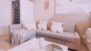 A modern living room with a beige sofa, white cushions, a coffee table, and a wall with a cloud mural. - “puff” Shinsaibashi Cloud House with Private Sauna (Osaka)
