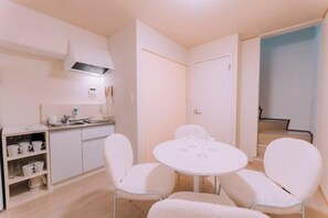 A compact kitchen with white cabinetry, a white dining table with four chairs, and a staircase leading to an upper level. - puff Shinsaibashi - Sauna, Projector, Sleeps 8 (Osaka)