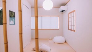 A minimalist room with a tatami mat floor, a shoji screen door, a white pillow, and a hanging light fixture. - “puff” Shinsaibashi Cloud House with Private Sauna (Osaka)